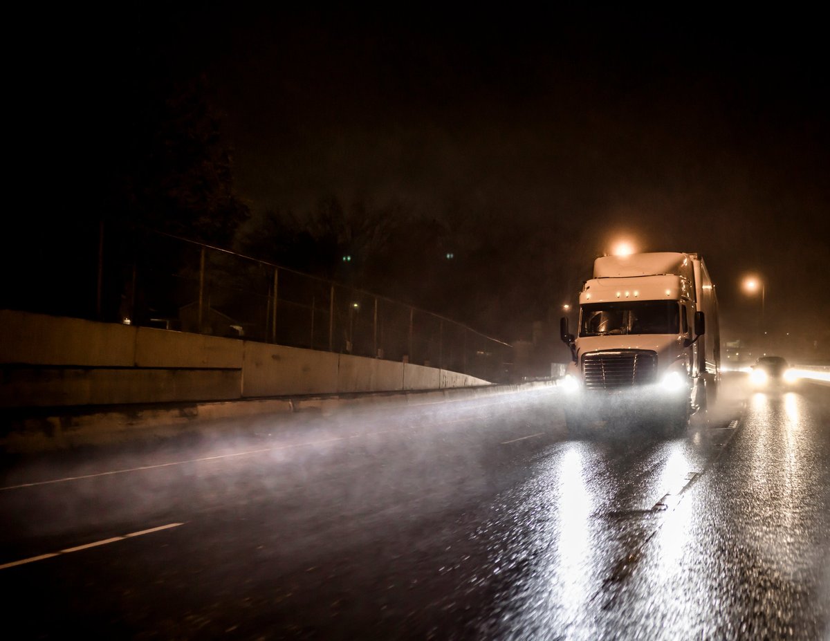 Semi truck with trailer transporting cargo at night on wet road with headlights