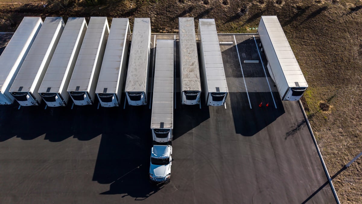 Aerial view of white semi trucks with refrigerated trailers parked at a warehouse lot representing trailers and dry boxes